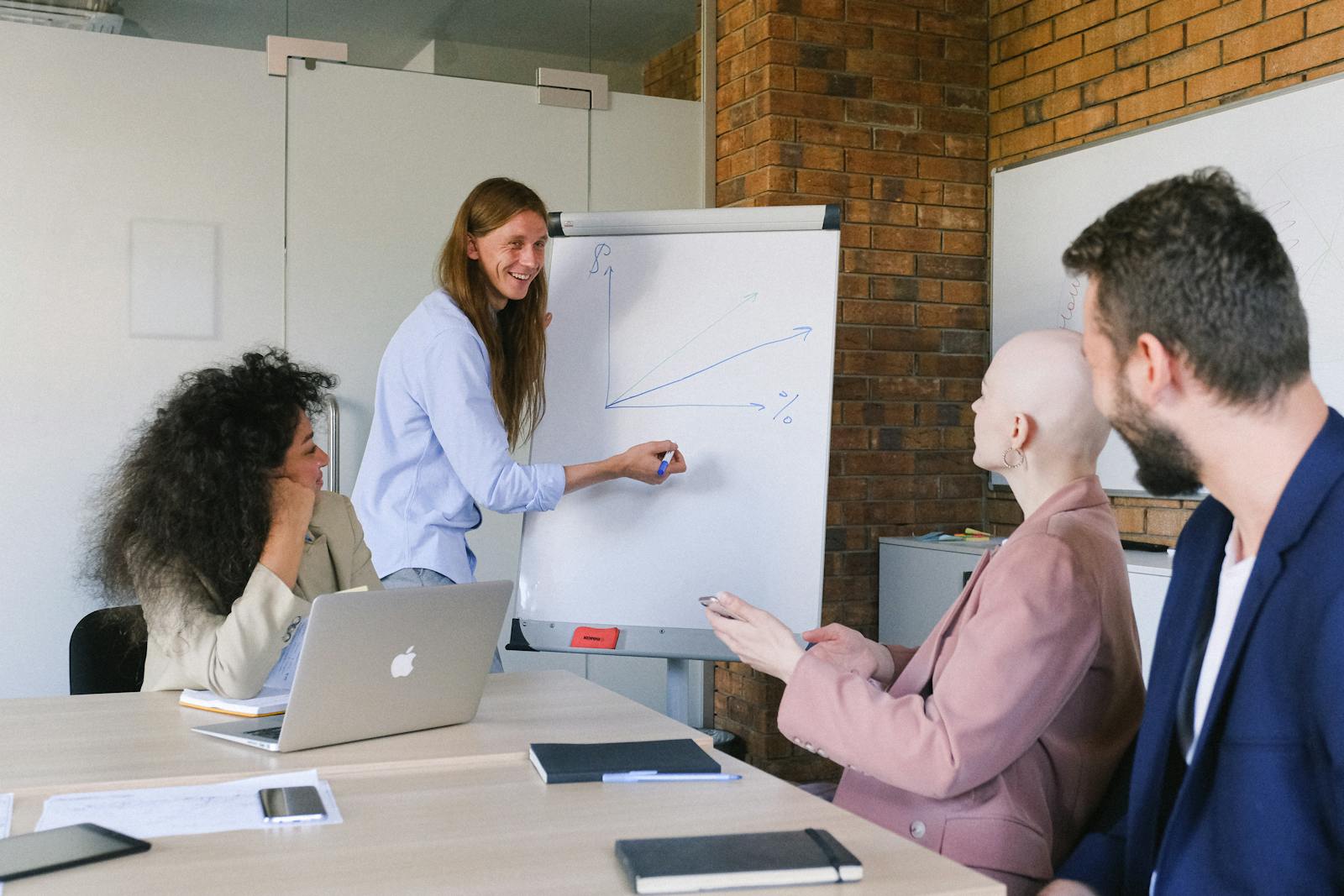 Smiling speaker drawing graph on whiteboard while explaining details of project to coworkers in modern workspace in daytime